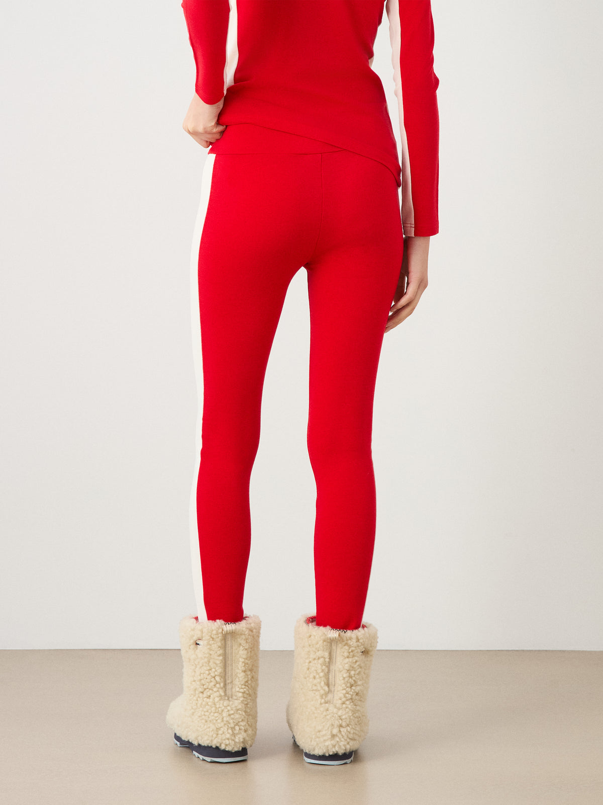 Back view of a person wearing We Norwegians Voss Leggings Women in red with white side stripes and beige faux-shearling boots.