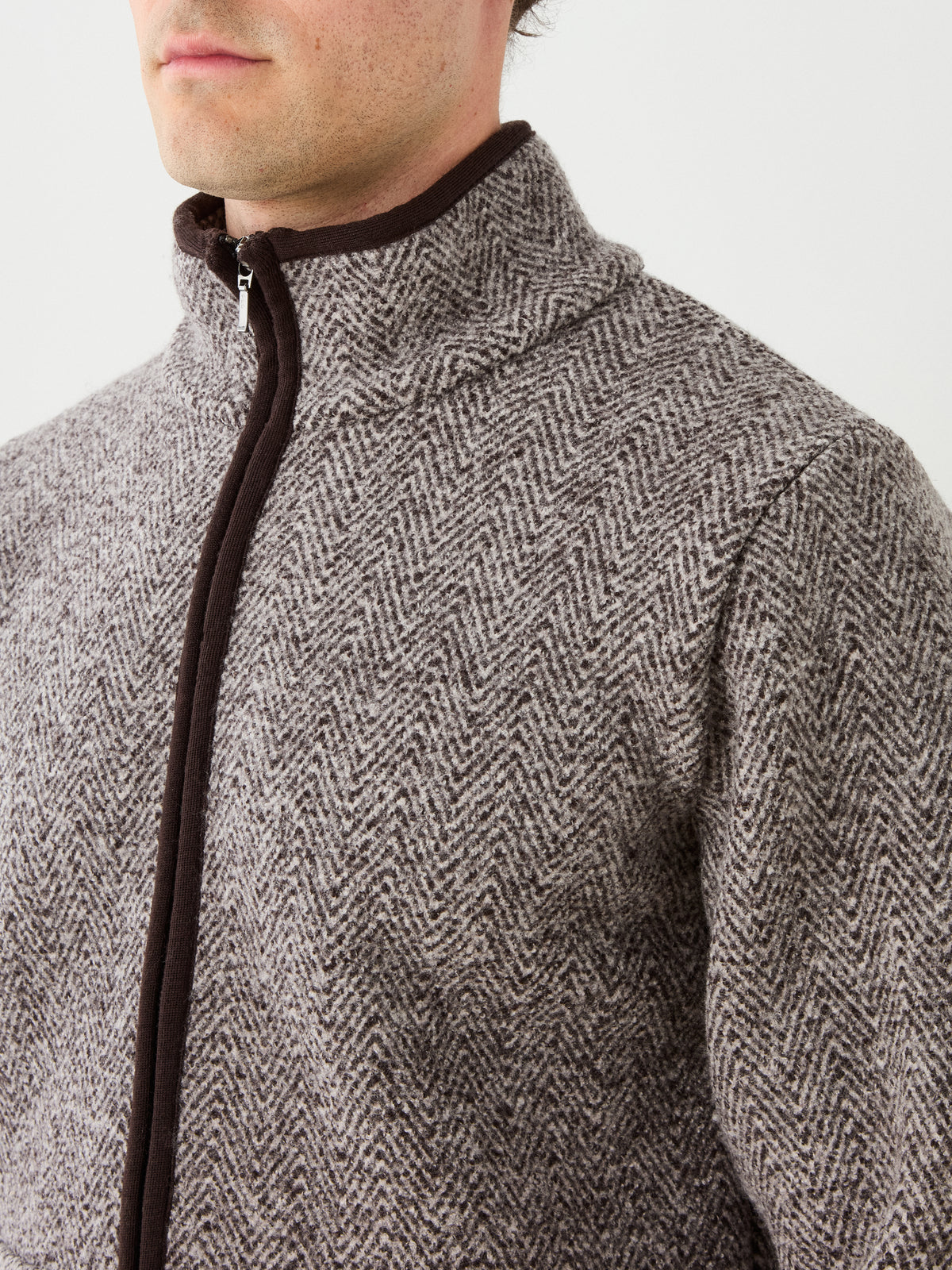 A person wearing the We Norwegians Laerdal Boiled Wool Jacket Men in a gray and white herringbone pattern with dark trim, shown from the shoulders to the chin against a plain light background, reflects understated Scandinavian craftsmanship.