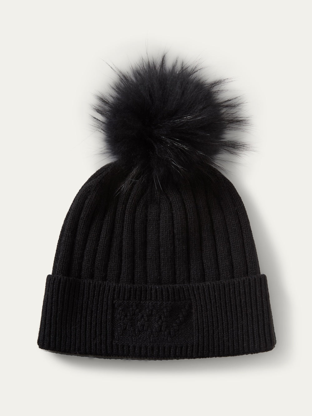 Black ribbed knit We Norwegians Geilo PomPom Hat featuring a large faux fur pom-pom on top and a square patch on the folded cuff.