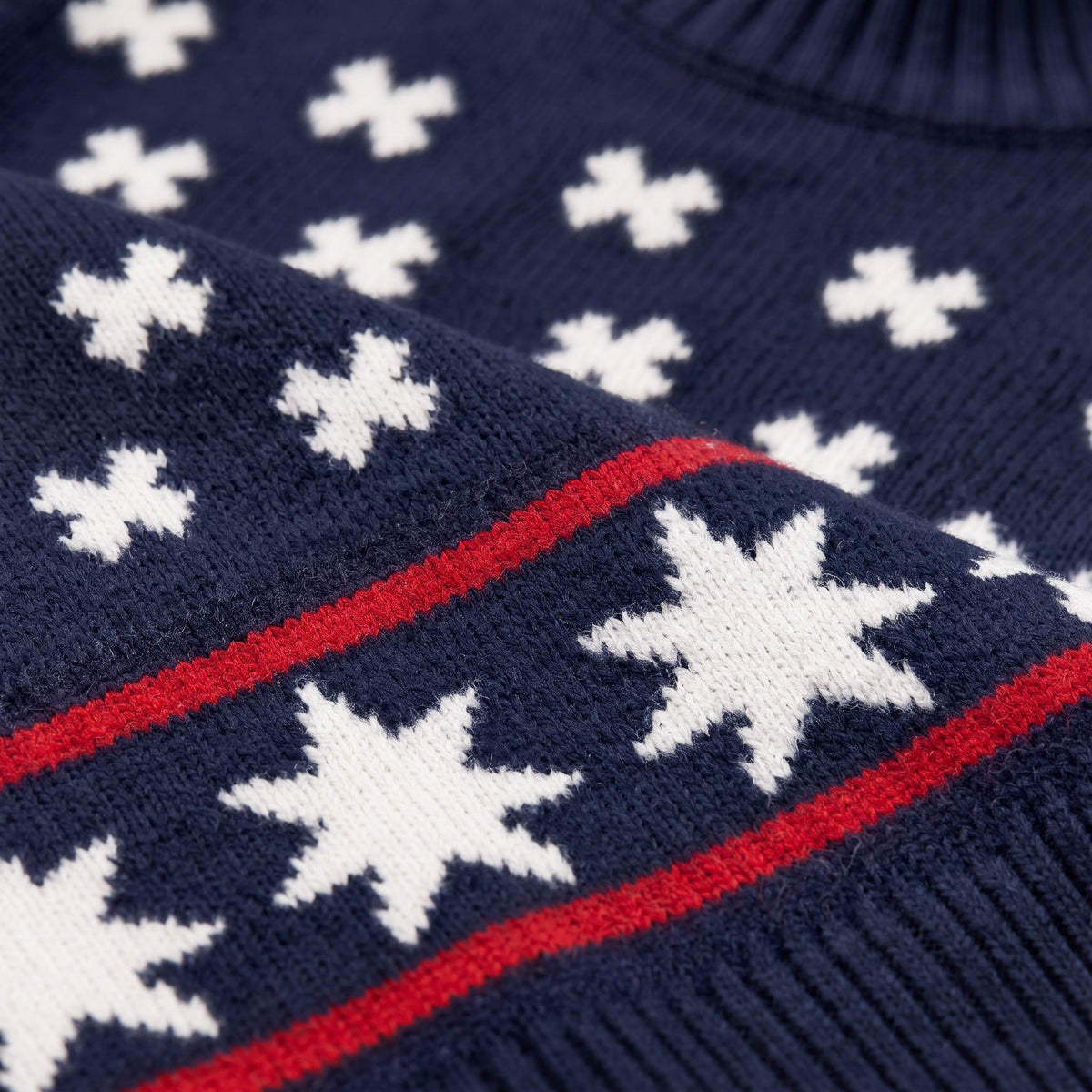 Close-up of the We Norwegians EMU x WN Sweater Women in navy blue knit, featuring white star and cross patterns with two parallel red stripes running horizontally between the star motifs.