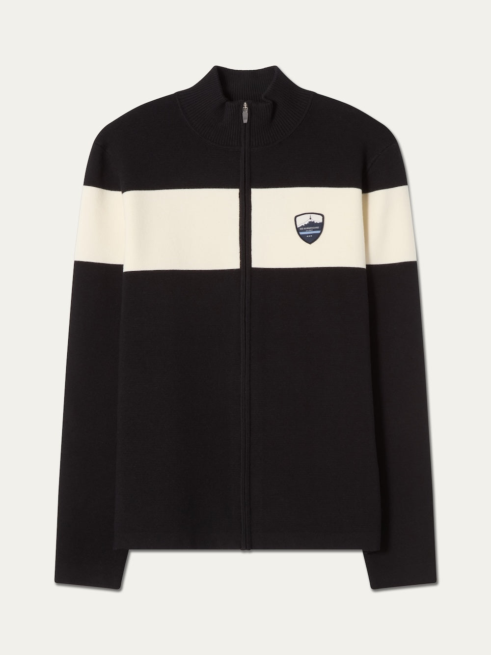 The We Norwegians Holmenkollen Full Zip Men is a black zip-up jacket with a white horizontal stripe across the chest and sleeves, accented by a small shield-shaped logo patch on the left chest. Inspired by Scandinavian mountain heritage, this jacket features a ribbed collar and straight hem for a classic look.