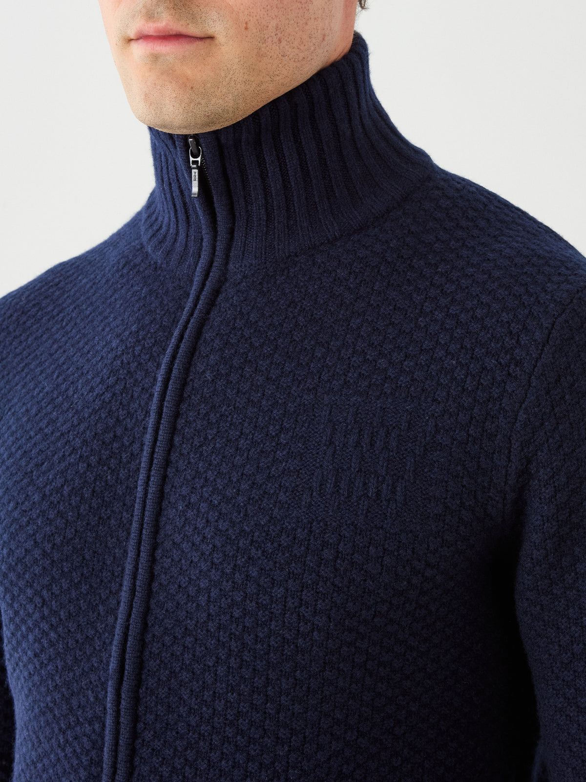 A person wearing the We Norwegians Kikut FullZip Men, a textured navy blue merino wool cardigan with a high collar. The photo is cropped to show only the lower face, neck, shoulders, and upper chest.
