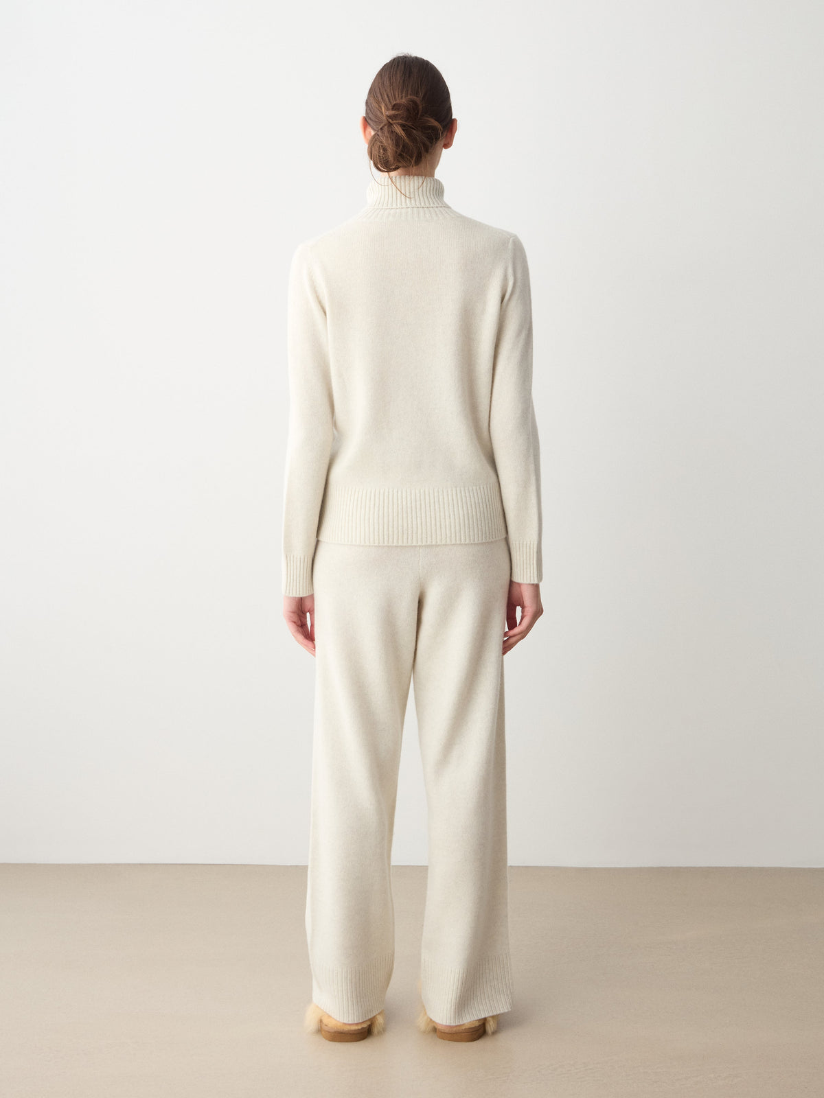 Back view of a person wearing a cream-colored We Norwegians Monogram Cashmere Sweater and matching wide-leg trousers.