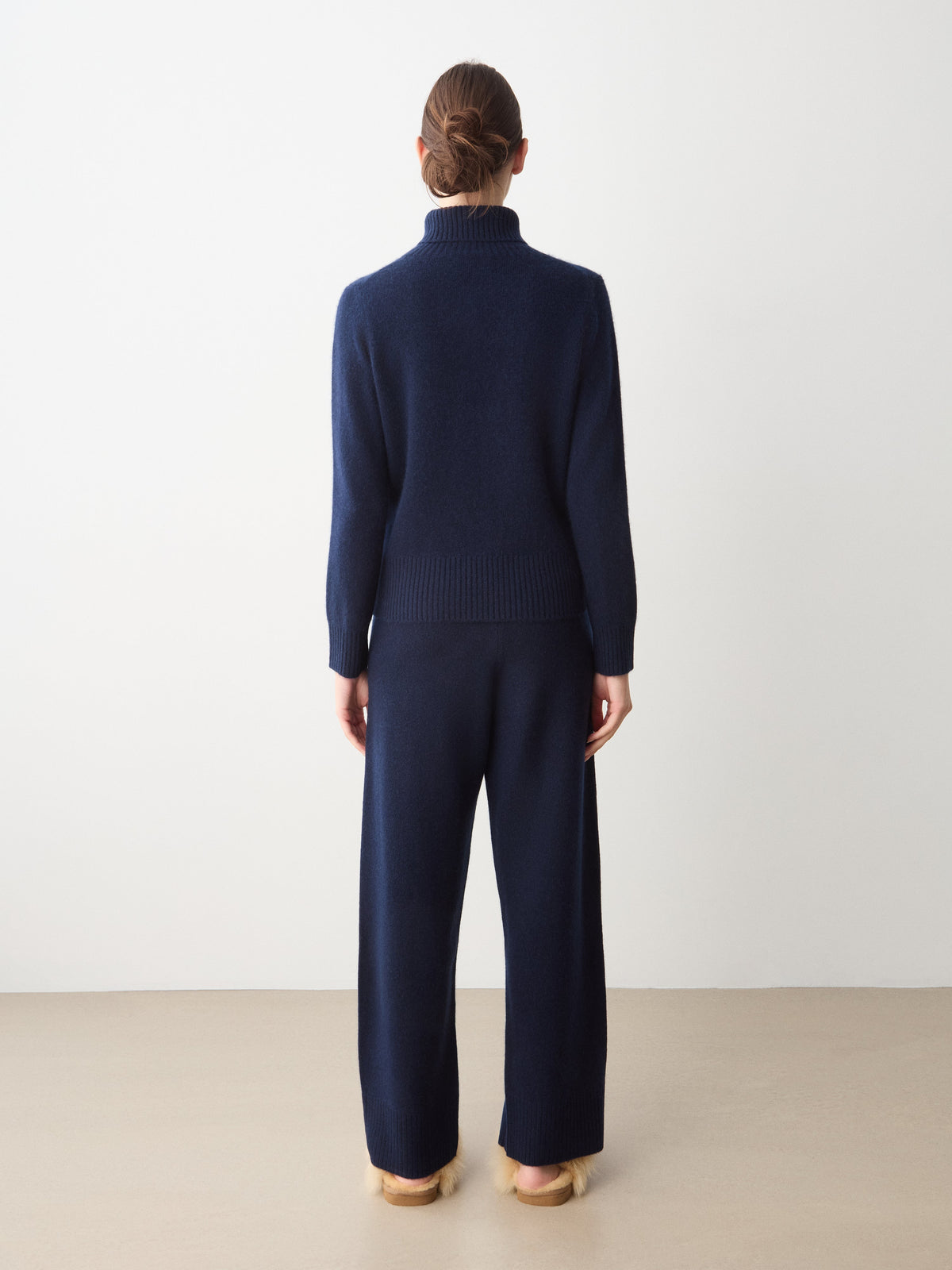 A person seen from behind wearing a dark blue Monogram Cashmere Sweater Women with matching wide-leg knit pants and tan slippers.
