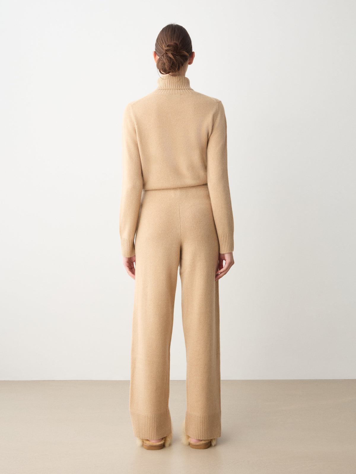 A person seen from behind wears a beige long-sleeved turtleneck sweater and matching Monogram Jogger Women cashmere pants for luxury loungewear.