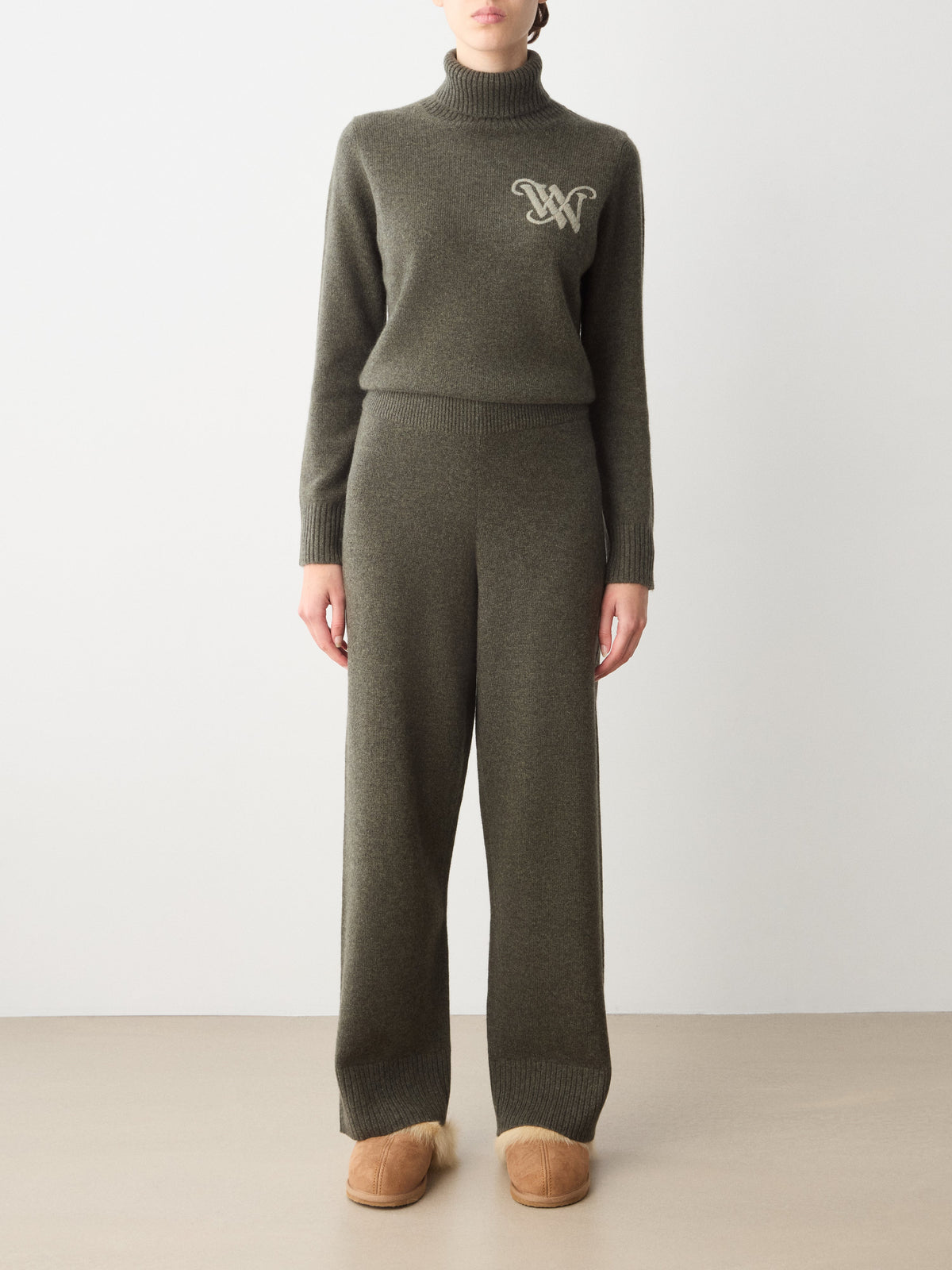 A person wearing a dark olive green turtleneck sweater with an embroidered logo and matching Monogram Jogger Women wide-leg knit pants, perfect as luxury loungewear.