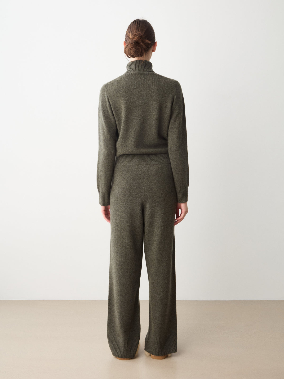Back view of a person wearing an olive green turtleneck sweater and matching We Norwegians Monogram Jogger Women cashmere pants for comfortable travel wear.