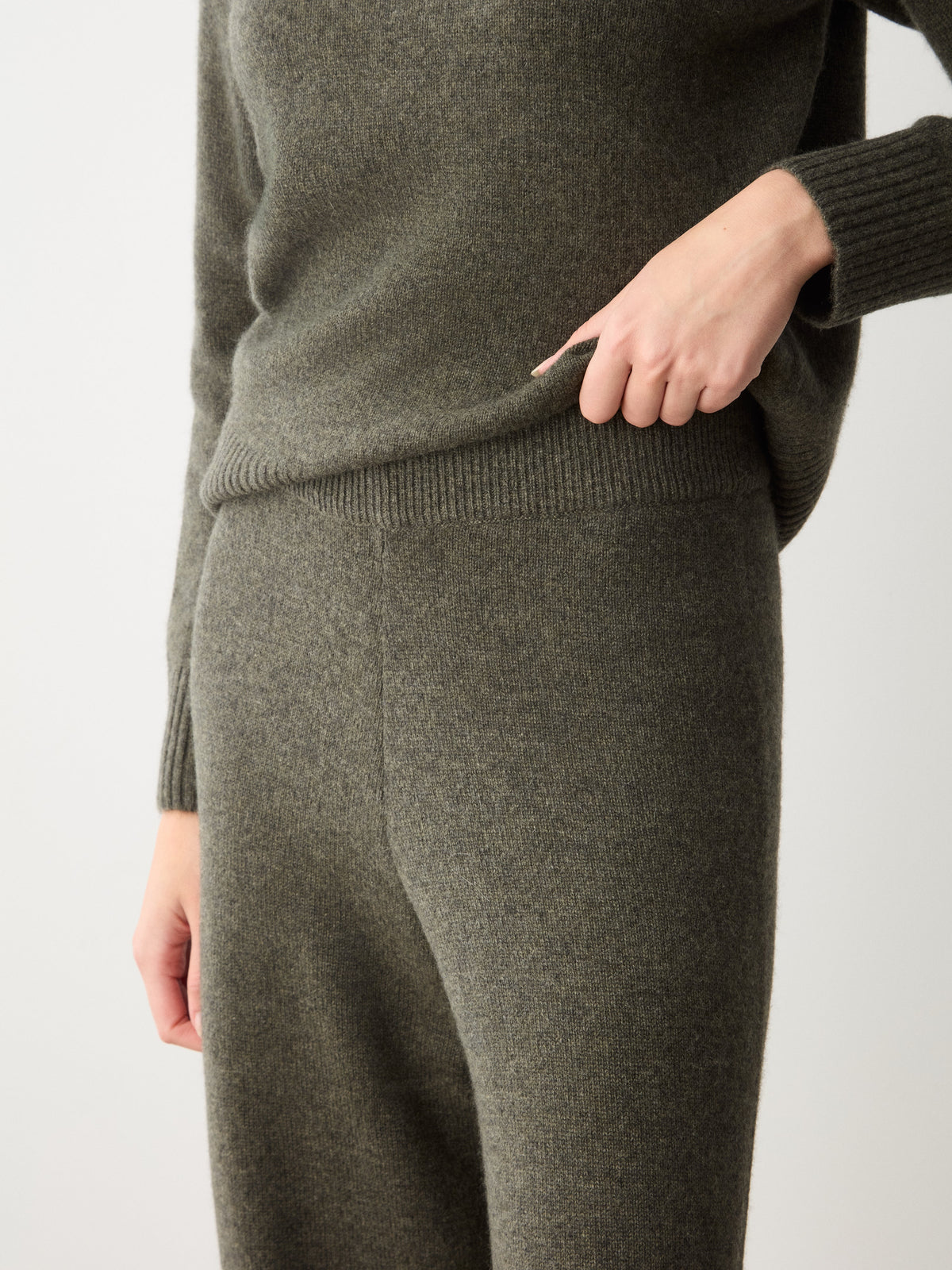 A person wearing dark olive cashmere Monogram Jogger Women sweatpants and a matching sweater for comfortable travel wear.