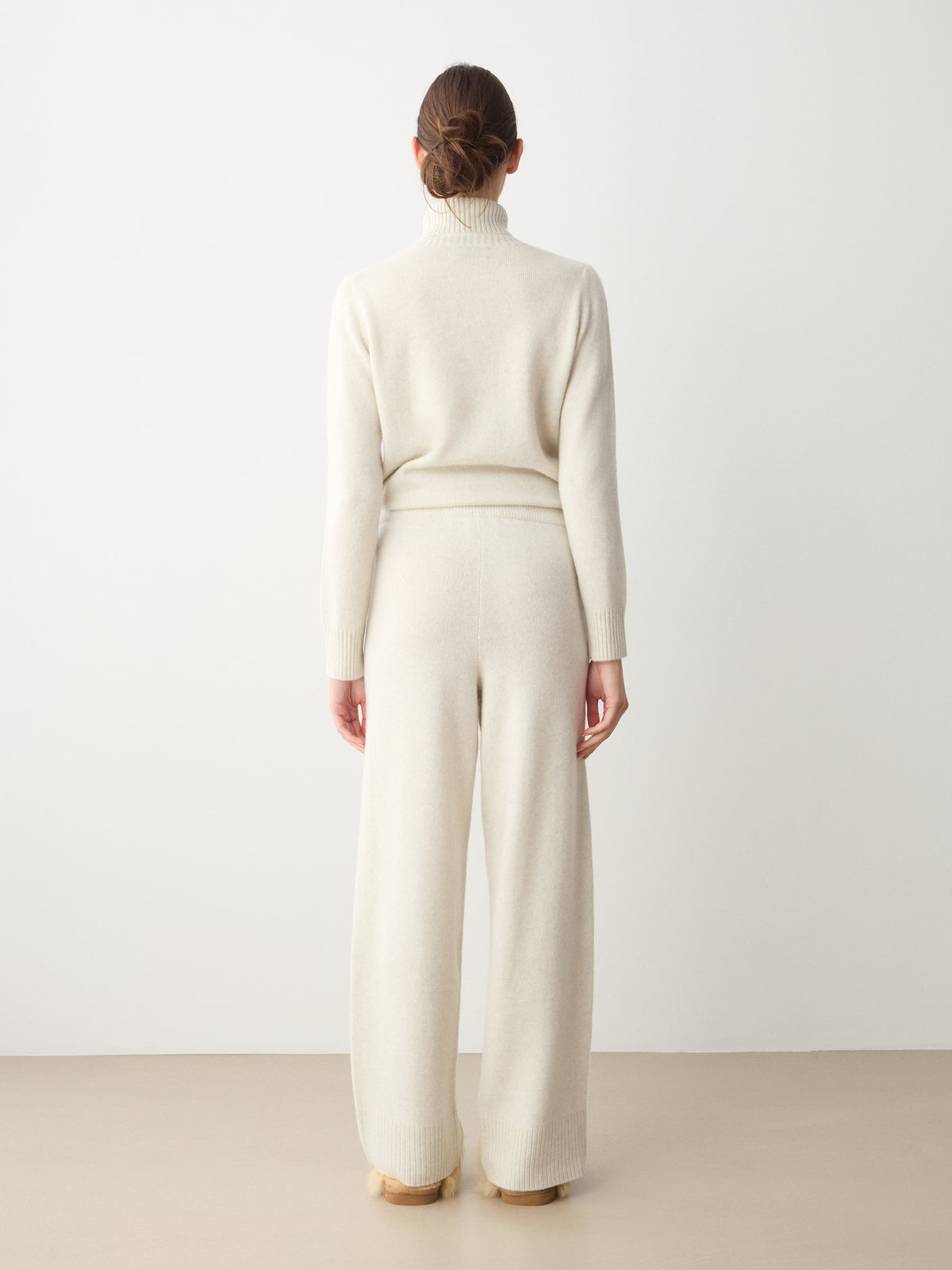 Back view of a person wearing a cream-colored turtleneck sweater and matching Monogram Jogger Women cashmere pants for comfortable travel wear.