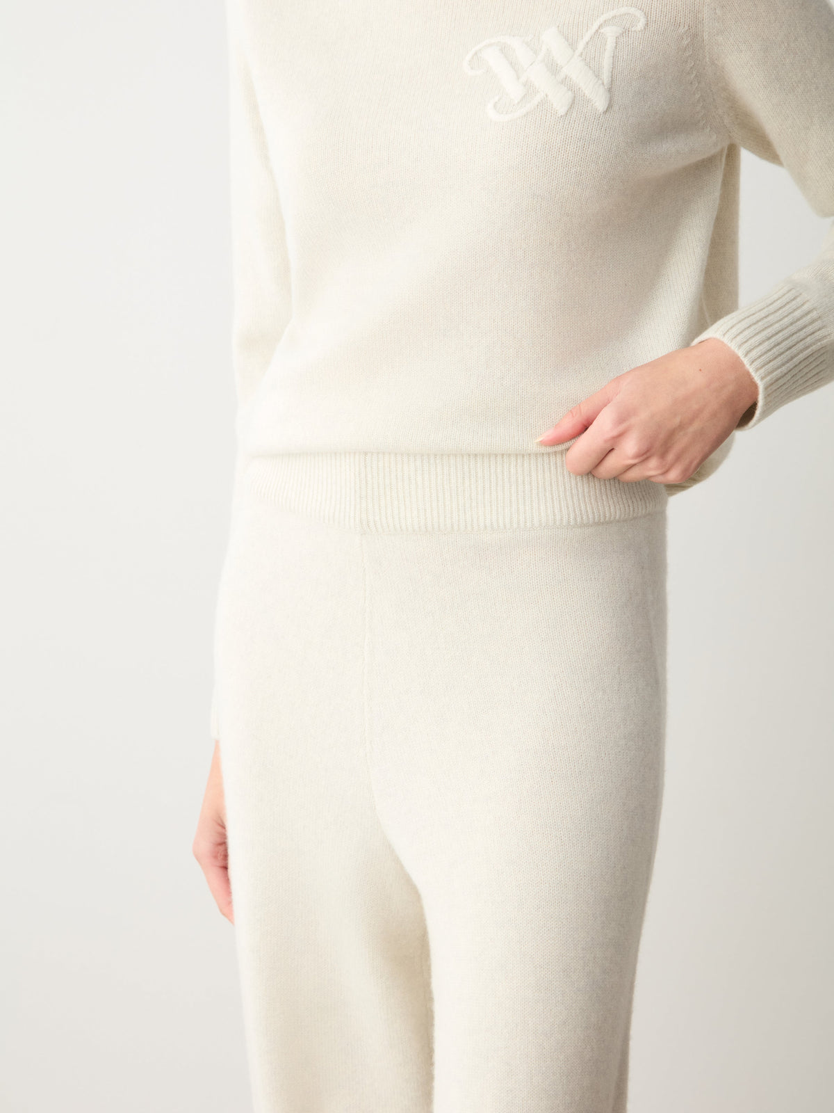 A person wearing a cream-colored Monogram Jogger Women sweater with a tonal monogram on the chest and matching luxury loungewear knit joggers.