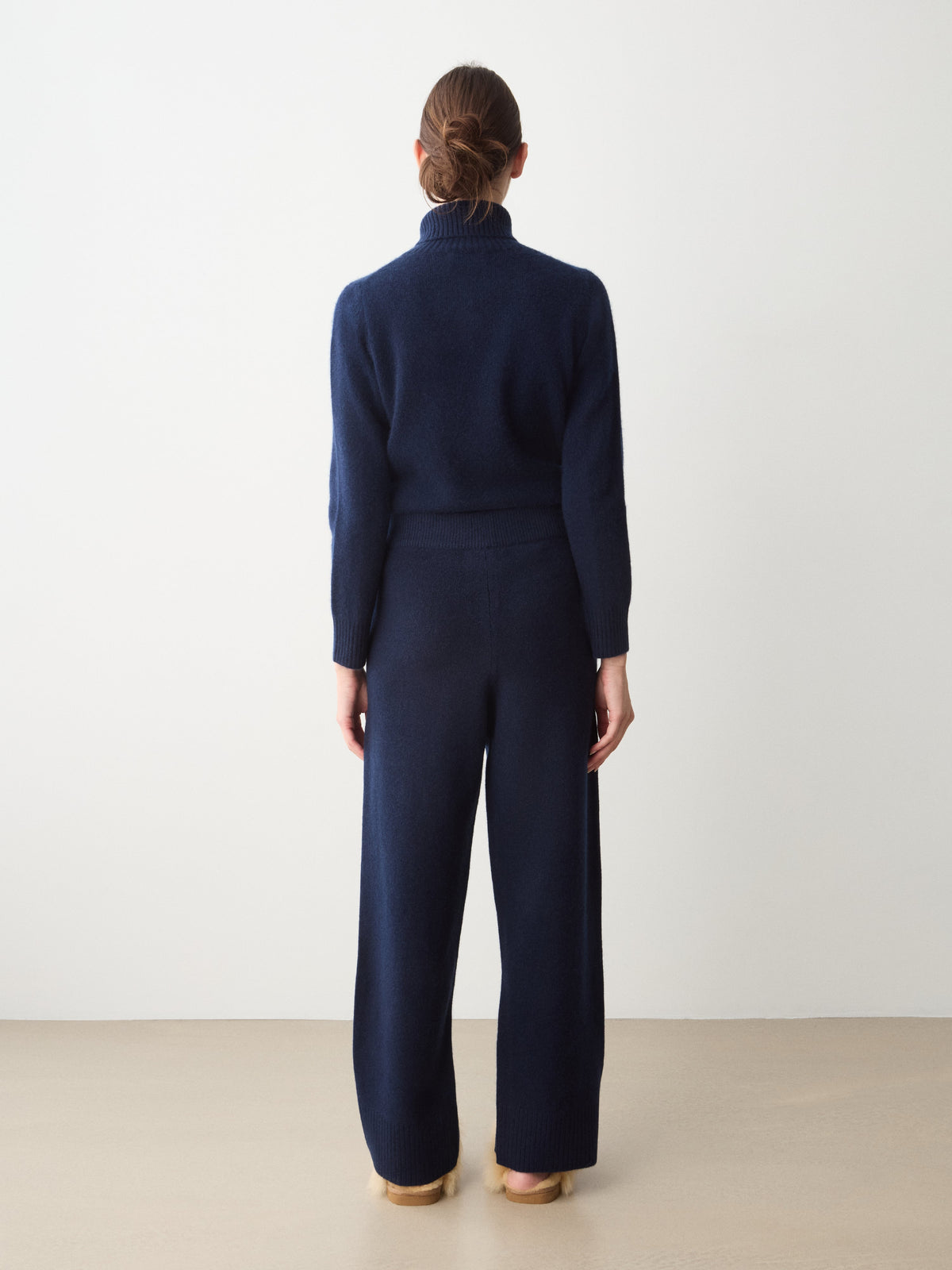Rear view of a person wearing the navy blue Monogram Jogger Women turtleneck sweater and matching relaxed-fit wide-leg trousers.