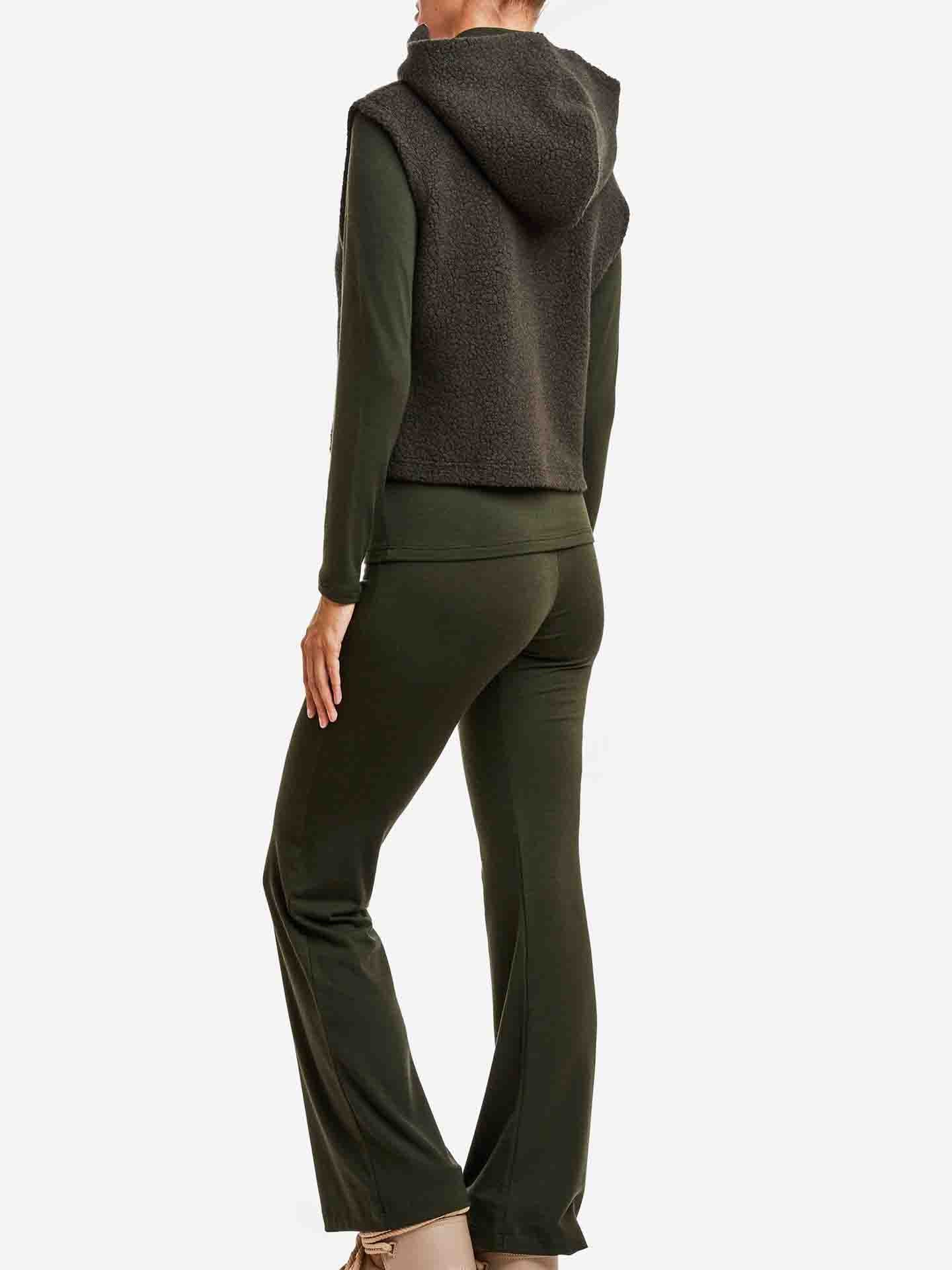 A person wearing a dark green outfit from the We Norwegians Alta collection, including a Merino wool long-sleeve top, pants, and the "Alta Hooded Vest Women," stands facing away from the camera. The casual and comfortable ensemble is paired with beige shoes against a white background.