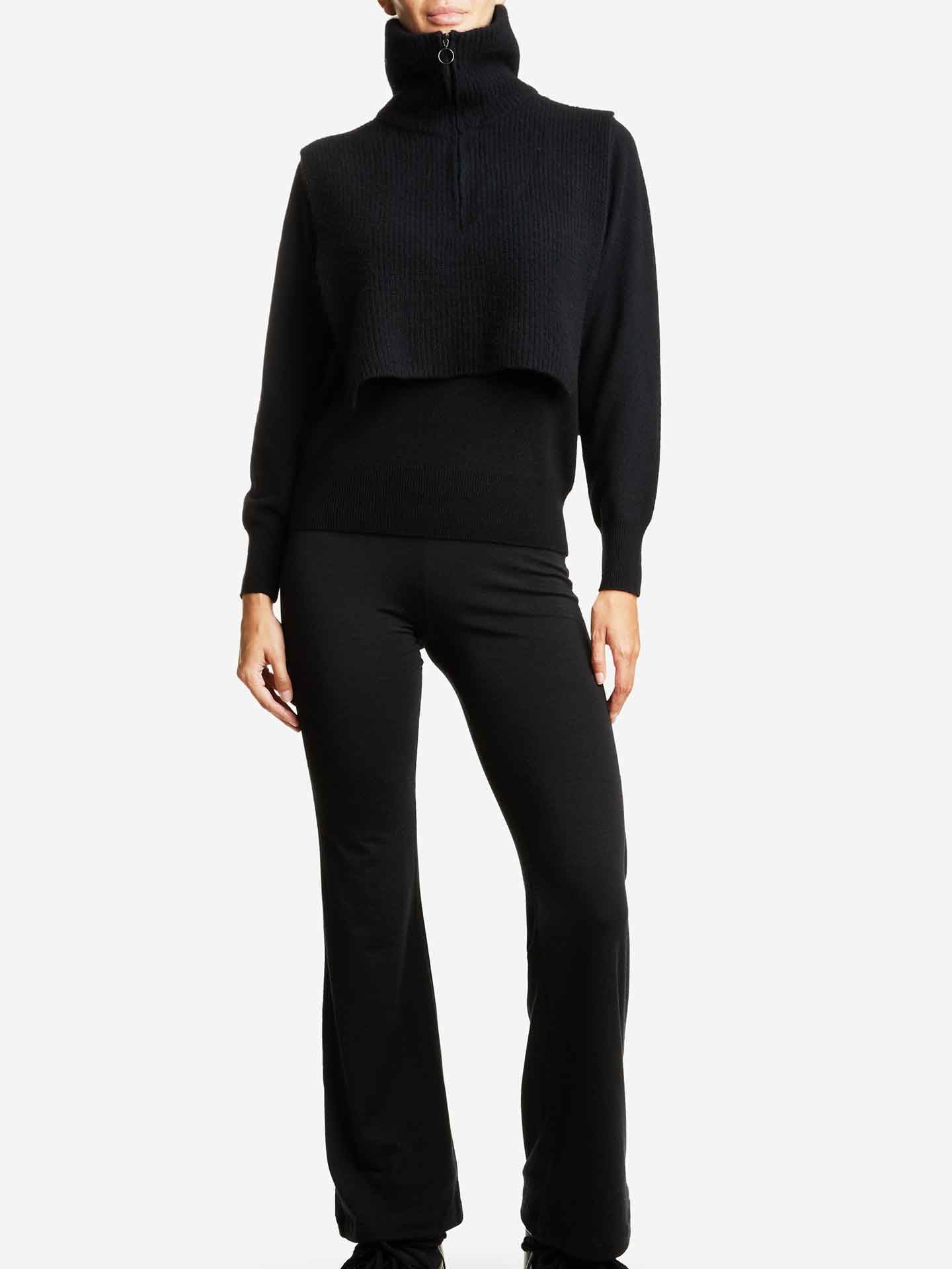 A person wearing a We Norwegians black turtleneck sweater paired with the Blefjell Cashmere Bib Women and black pants stands against a plain white background.