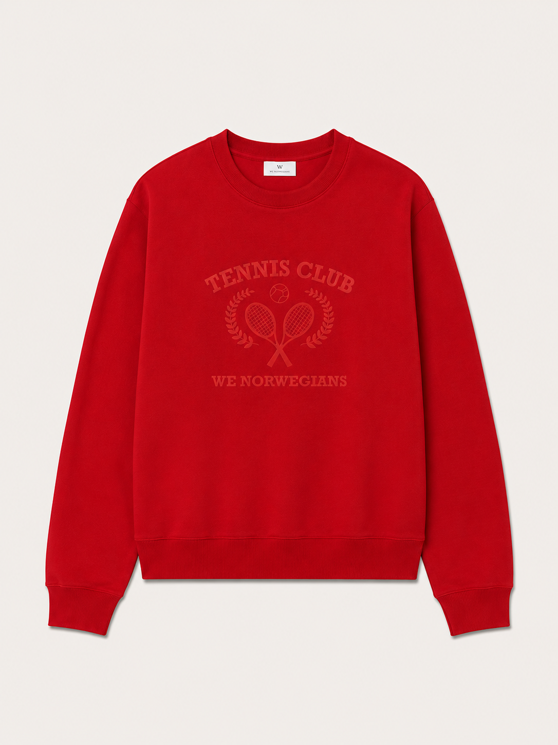 The Chelsea Sweater Women by We Norwegians is a red cotton jersey crew neck with an embossed design of crossed tennis rackets, laurel branches, and the words “TENNIS CLUB” above and “WE NORWEGIANS” below.