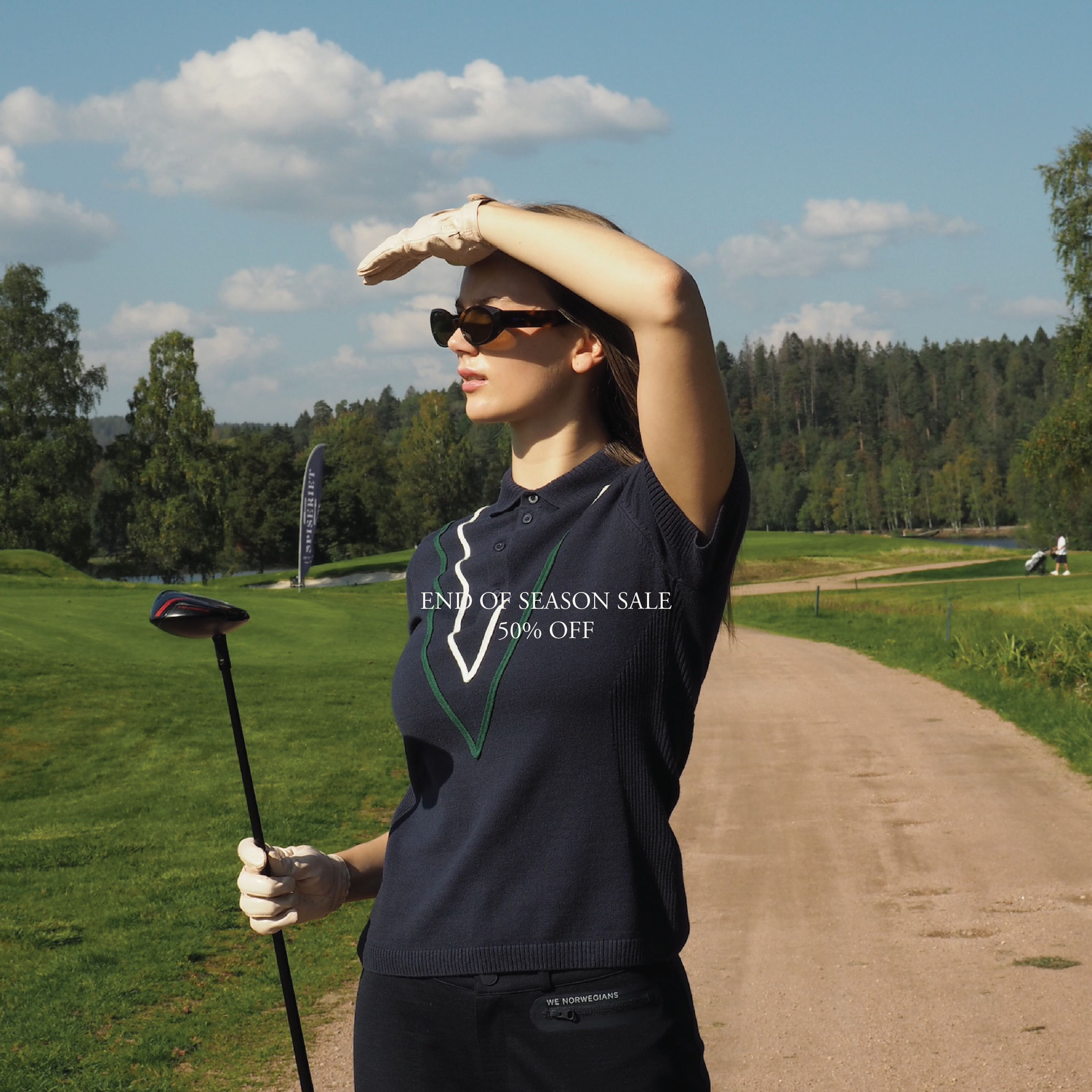 We Norwegians_SS25_Model is wearing Team Chevron Polo with Ace Pants_Navy blue_Standing in a golf course