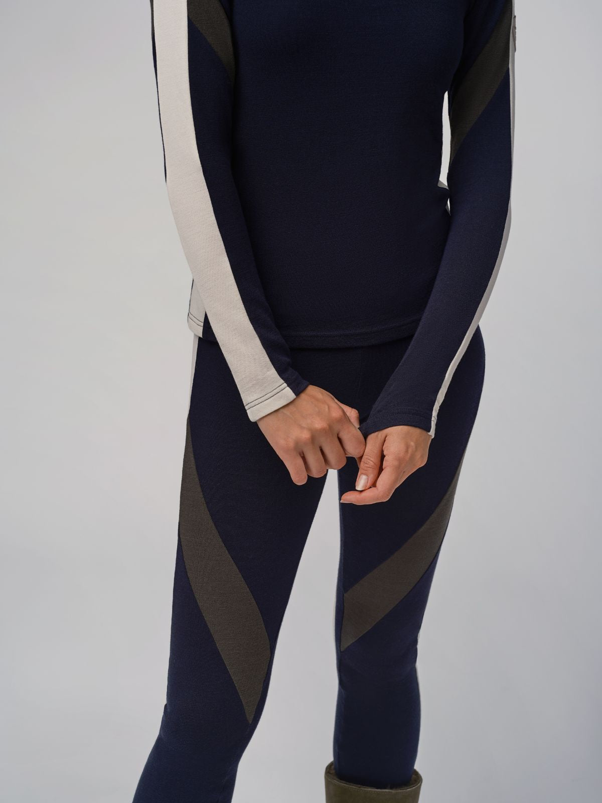 A person showcases the We Norwegians Inuikii+WN Leggings Women, featuring a navy blue and dark green athletic outfit with white stripes. Made from cozy Merino wool, this ensemble includes a long-sleeve shirt and matching leggings, ideal for ski fashionistas. They are photographed against a plain background with their head unseen in the image.