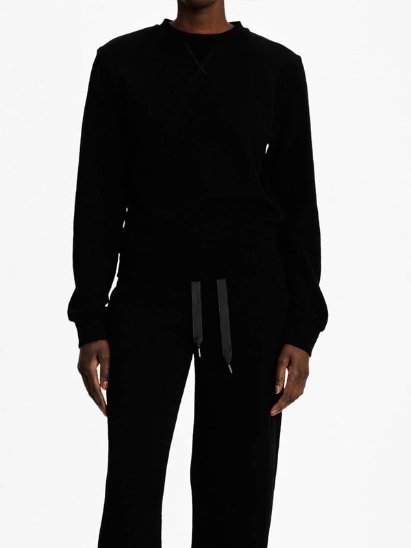 A person is wearing the Tind Crewneck Women shirt by We Norwegians along with black drawstring pants, embodying a luxurious sporty style while standing against a plain white background. The head is not visible in the image.