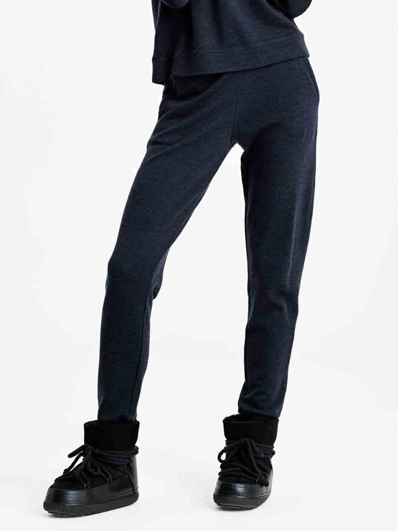 A person wearing the Tind Jogger Women by We Norwegians in dark blue, paired with black high-top sneakers featuring thick soles, exudes an off-duty style. The individual is standing against a plain white background, with their upper body partially out of frame.