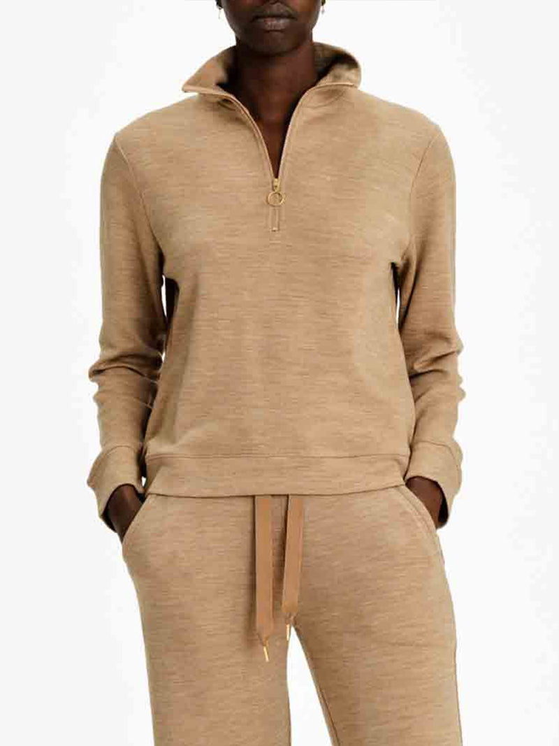 A person is wearing the Tind Zip Up Sweater Women by We Norwegians, a beige, long-sleeve, half-zip pullover with a standing collar and matching drawstring pants made from soft Merino wool sportswear. Their hands are in their pants' pockets, and the background is plain white.