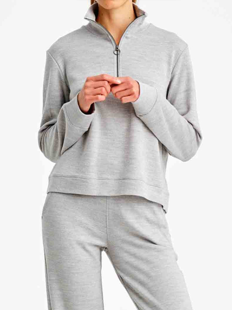 A person is standing against a plain background, wearing the We Norwegians Limited Time Bundle: Tind Zip Up & Tind Jogger Women in light gray. Their hands are clasped together near their chest, and their head is cropped out of the frame.