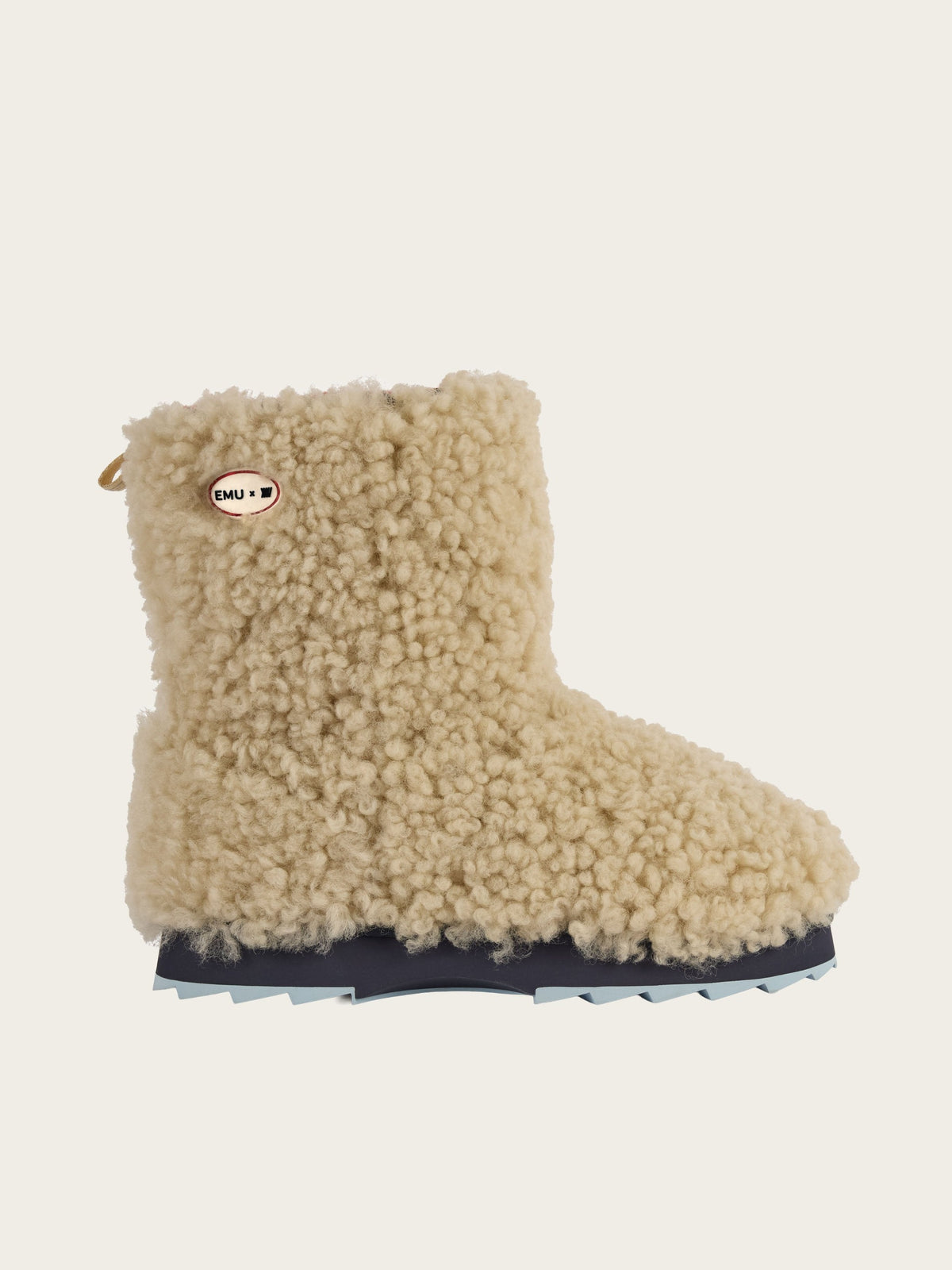 A single EMU x WN Sharky Lo Teddy boot by We Norwegians, featuring a beige, textured teddy sheepskin exterior, black-and-blue ridged sole, and a small oval tag near the ankle, displayed on a plain light background.