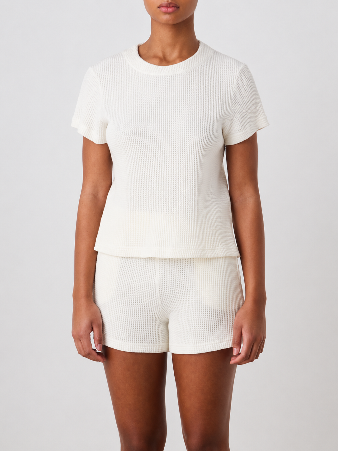 A person stands facing forward, wearing the We Norwegians Waffle Tee Women in a matching off-white set, against a plain light background.